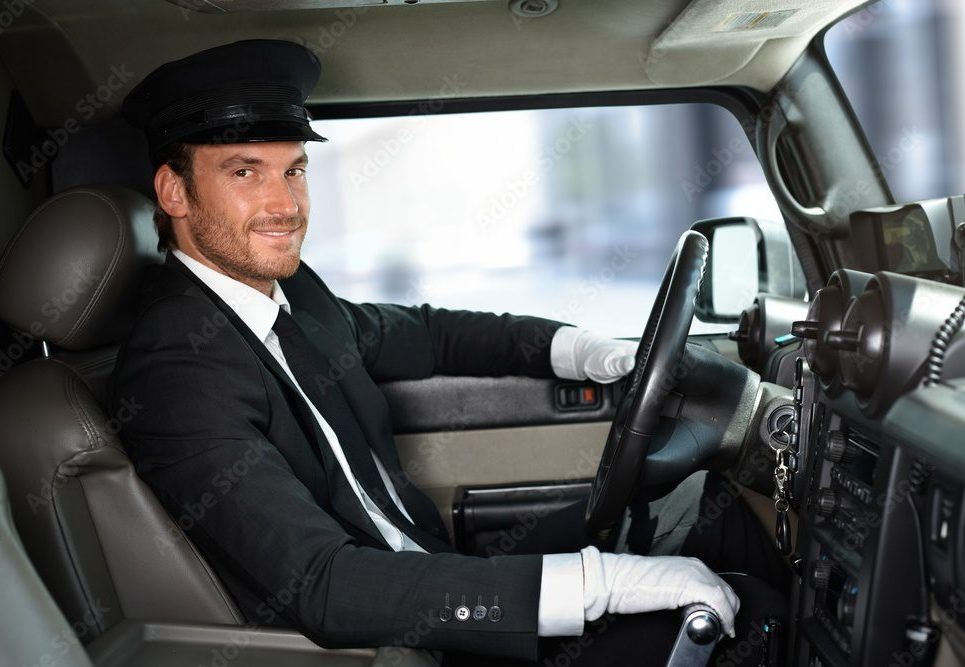 A professional uniformed chauffeur wearing a cap and white gloves smiling while driving a luxury vehicle, representing Gateway Limousine's premium drive-as-directed and executive car services in St. Louis.